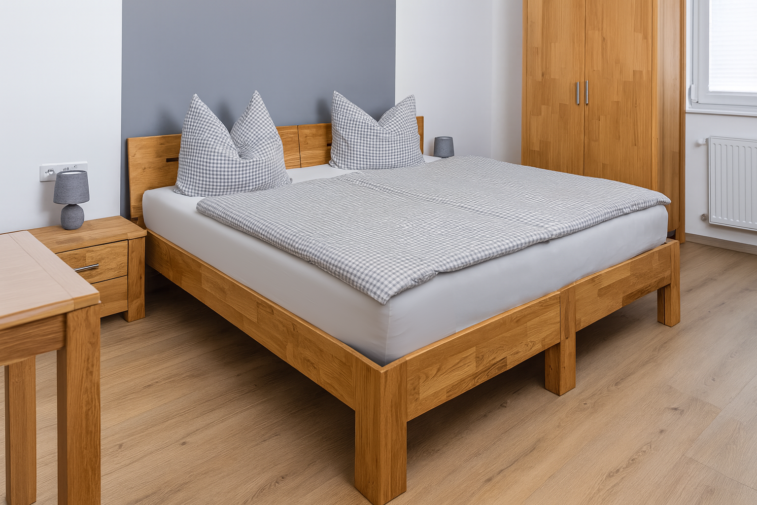 Bettgestell aus hellem Holz mit grauer, fein karierten Bettdecke und zwei großen karierten Kissen vor einer grauen Akzentwand; seitlich ein Nachttisch mit grauer Lampe, Holzkleiderschrank und heller Holzboden in einem schlichten, modernen Schlafzimmer.